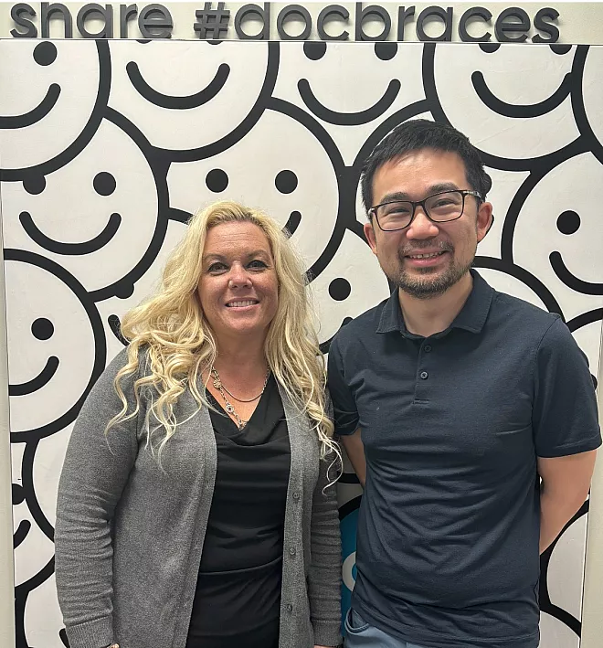 Image 123650291 - male and female standing in front of docbraces smile branded wall that reads share docbraces